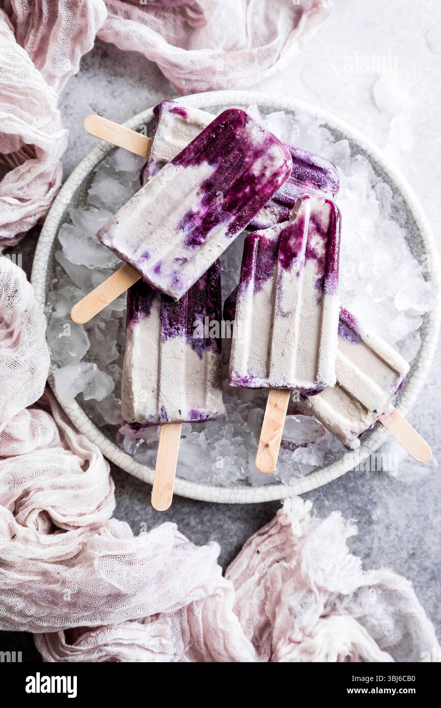 Une assiette de popsicles violettes et blanches reposant sur de la glace, entourée d'un tissu rose doux. Banque D'Images