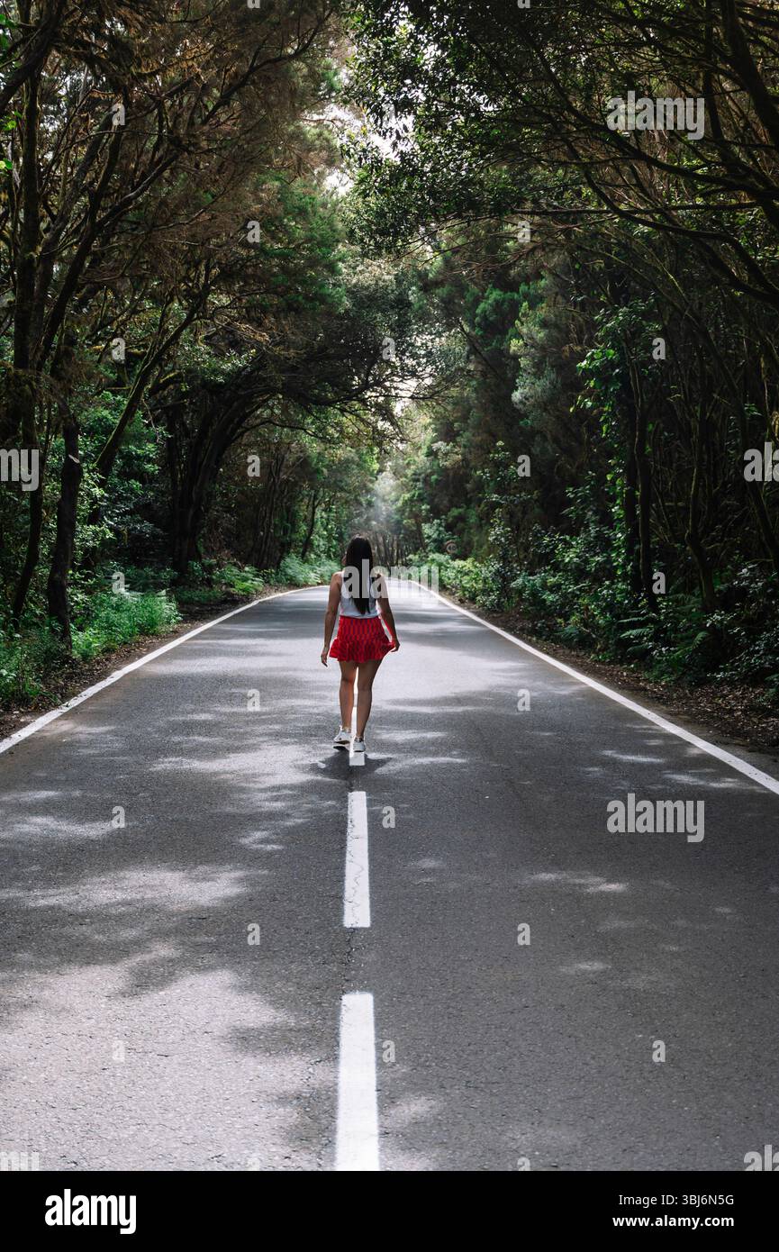 Une femme marche sur une route avec des arbres en arrière-plan. La route est vide et la femme est seule Banque D'Images