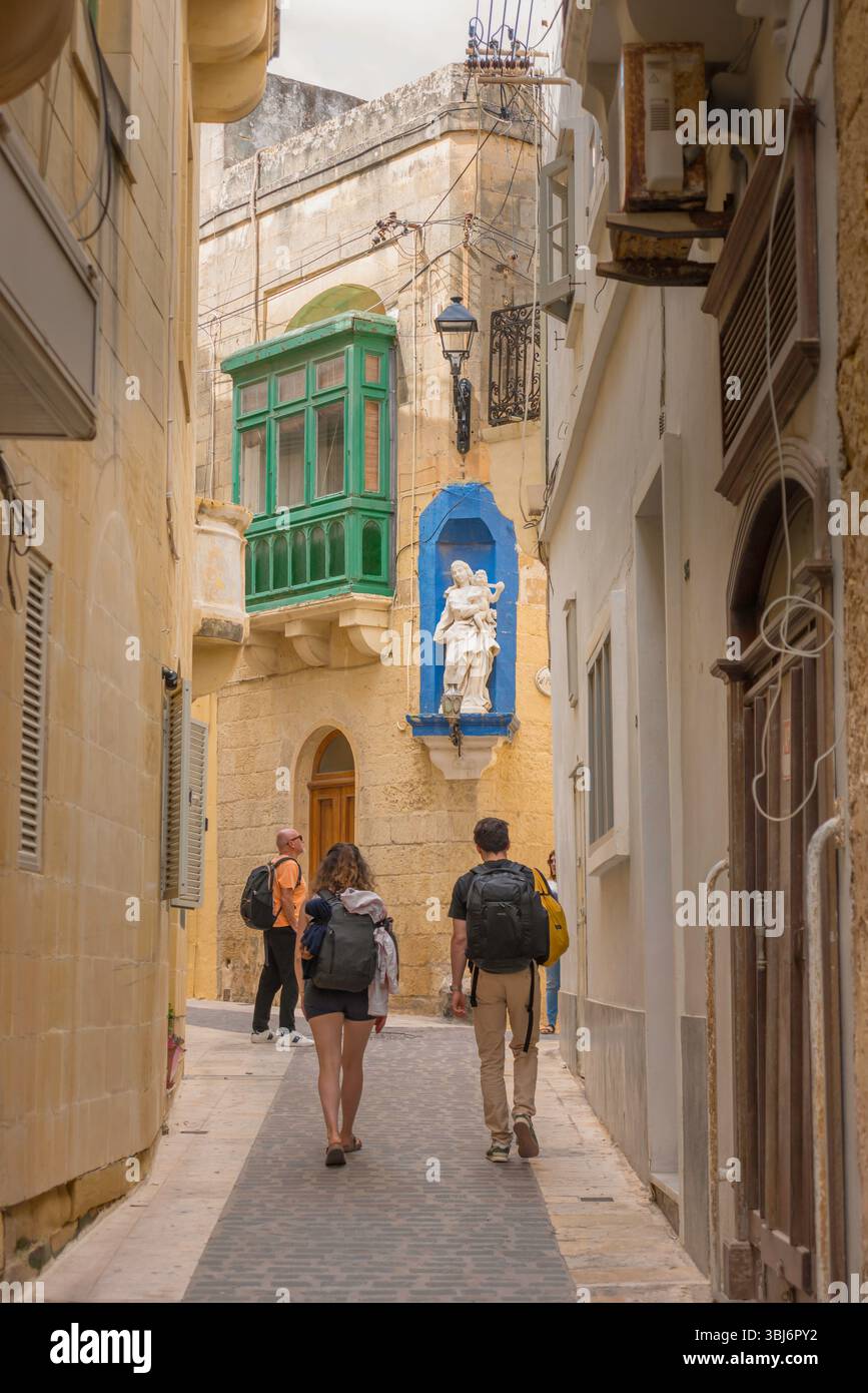 Voyage jeune couple, vue arrière de touristes portant des sacs à dos explorant un quartier dans le quartier pittoresque de la vieille ville de Victoria (Rabat), Gozo, Malte Banque D'Images