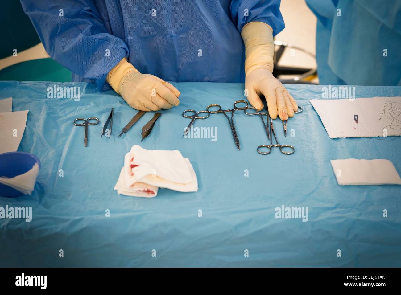 Infirmière assise sur la table d'un instrumentiste dans une salle d'opération de dermatologie, portant des gants et une blouse chirurgicale bleue, en plaçant l'instru chirurgical Banque D'Images
