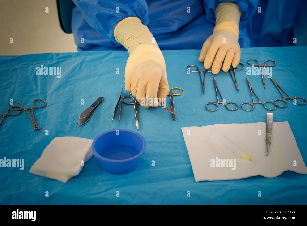 Infirmière assise sur la table d'un instrumentiste dans une salle d'opération de dermatologie, portant des gants et une blouse chirurgicale bleue, en plaçant l'instru chirurgical Banque D'Images