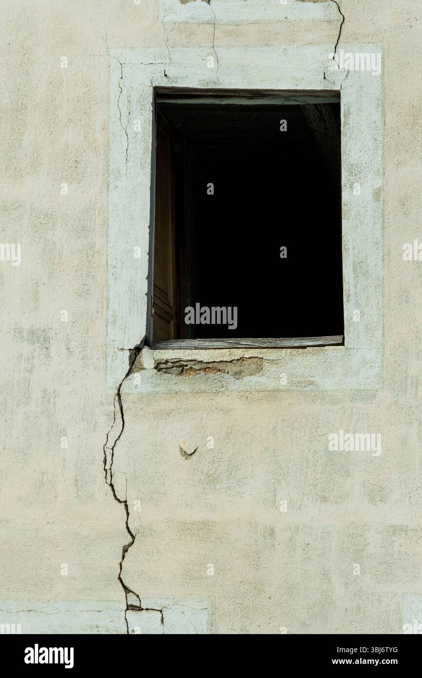 Mur fissuré et fenêtre vide sombre montrent la négligence d'une structure abandonnée. La peinture pelable suggère des années de détérioration Banque D'Images