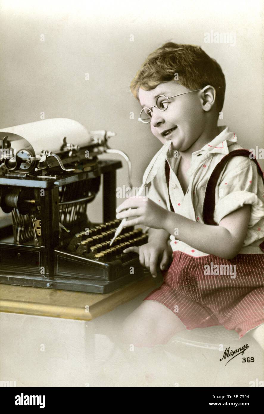 Garçon à la machine à écrire, 1920, garçon avec des lunettes jouant joyeusement à une vieille machine à écrire, il semble imaginer écrire, photo historique Banque D'Images