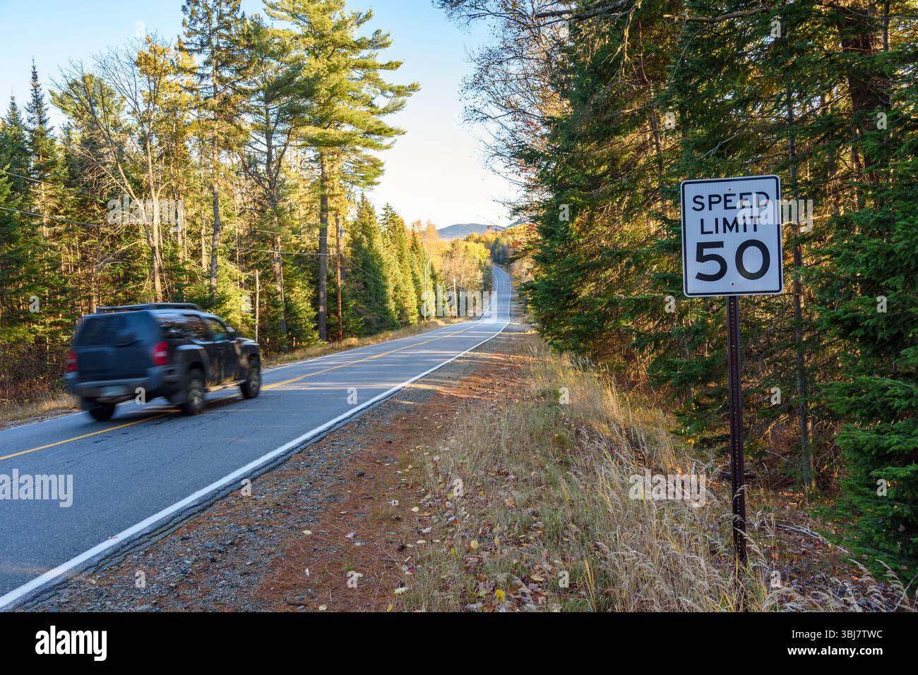 Voiture passant un panneau de limite de vitesse sur une route forestière dans la montagne au coucher du soleil en automne Banque D'Images
