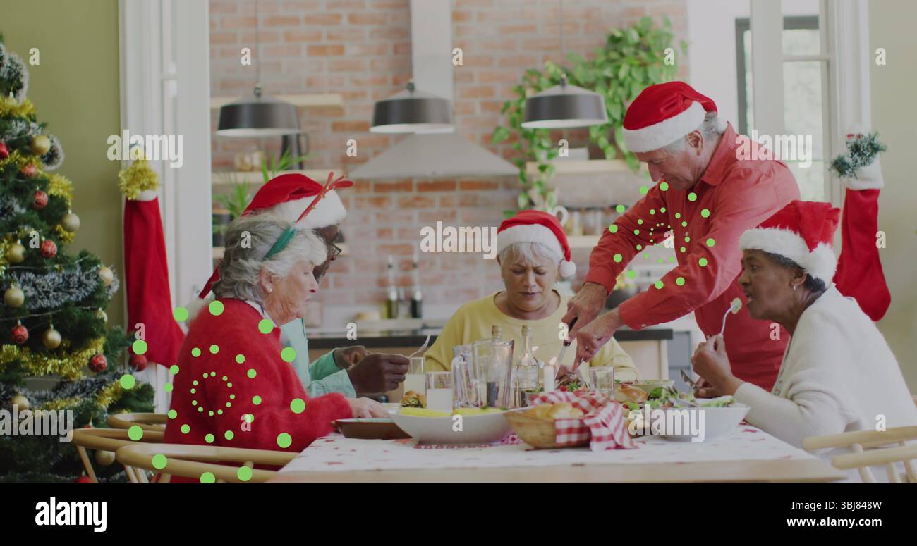 Groupe de cinq amis seniors partageant le repas de vacances à la table en bois dans la cuisine, avec chapeaux de Père Noël Banque D'Images