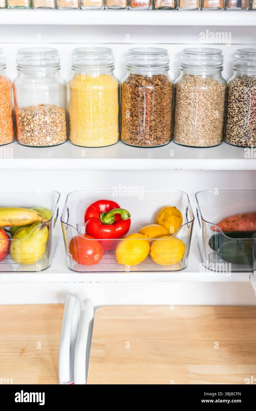 petit garde-manger organisé avec des bocaux transparents assortis remplis de céréales, légumineuses, épices et produits frais dans des récipients, alimentation saine, maison rangée, organi Banque D'Images