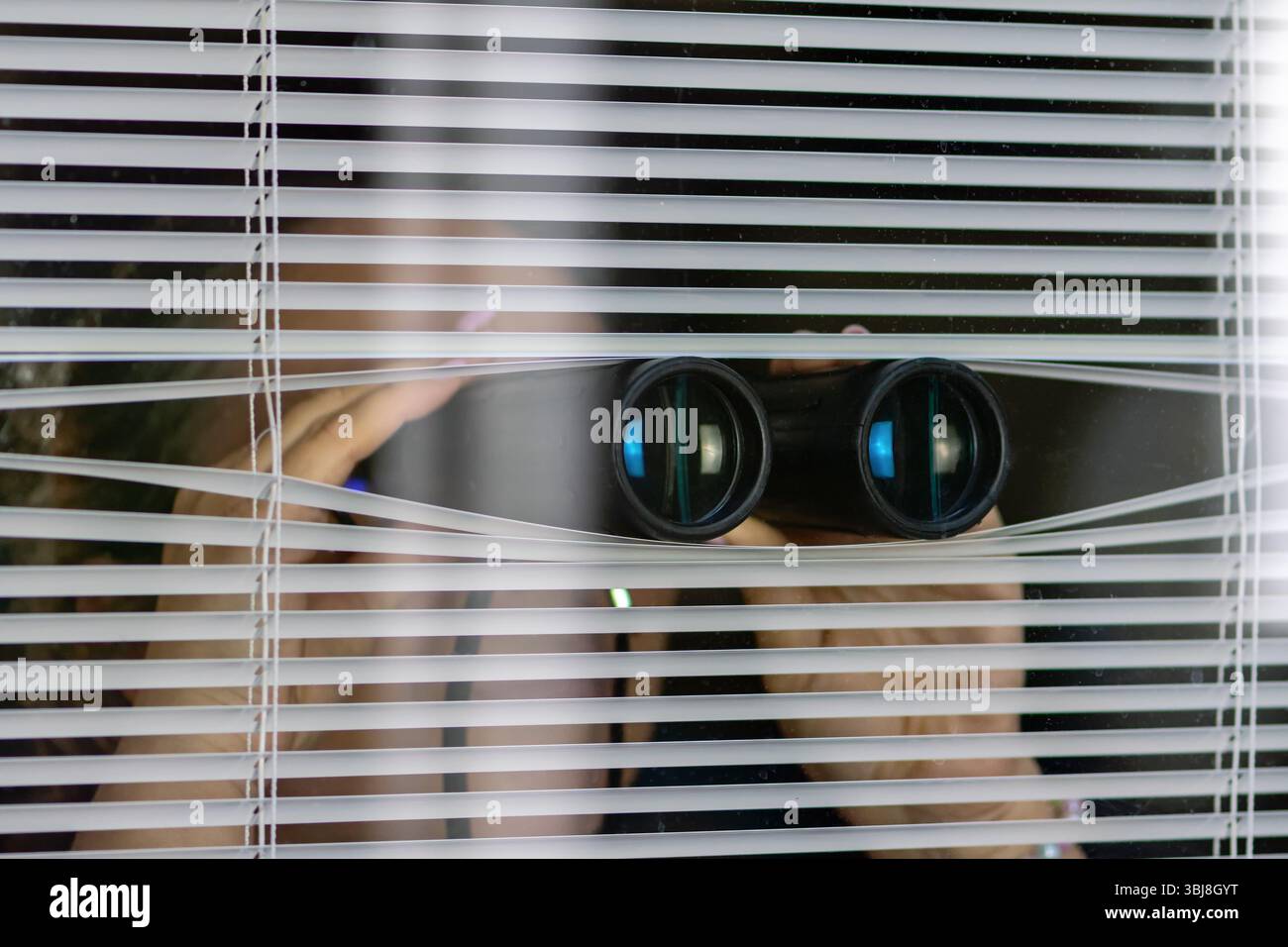 Un homme avec des jumelles observant à travers les stores. Le concept de surveillance, d'espionnage ou de surveillance secrète Banque D'Images