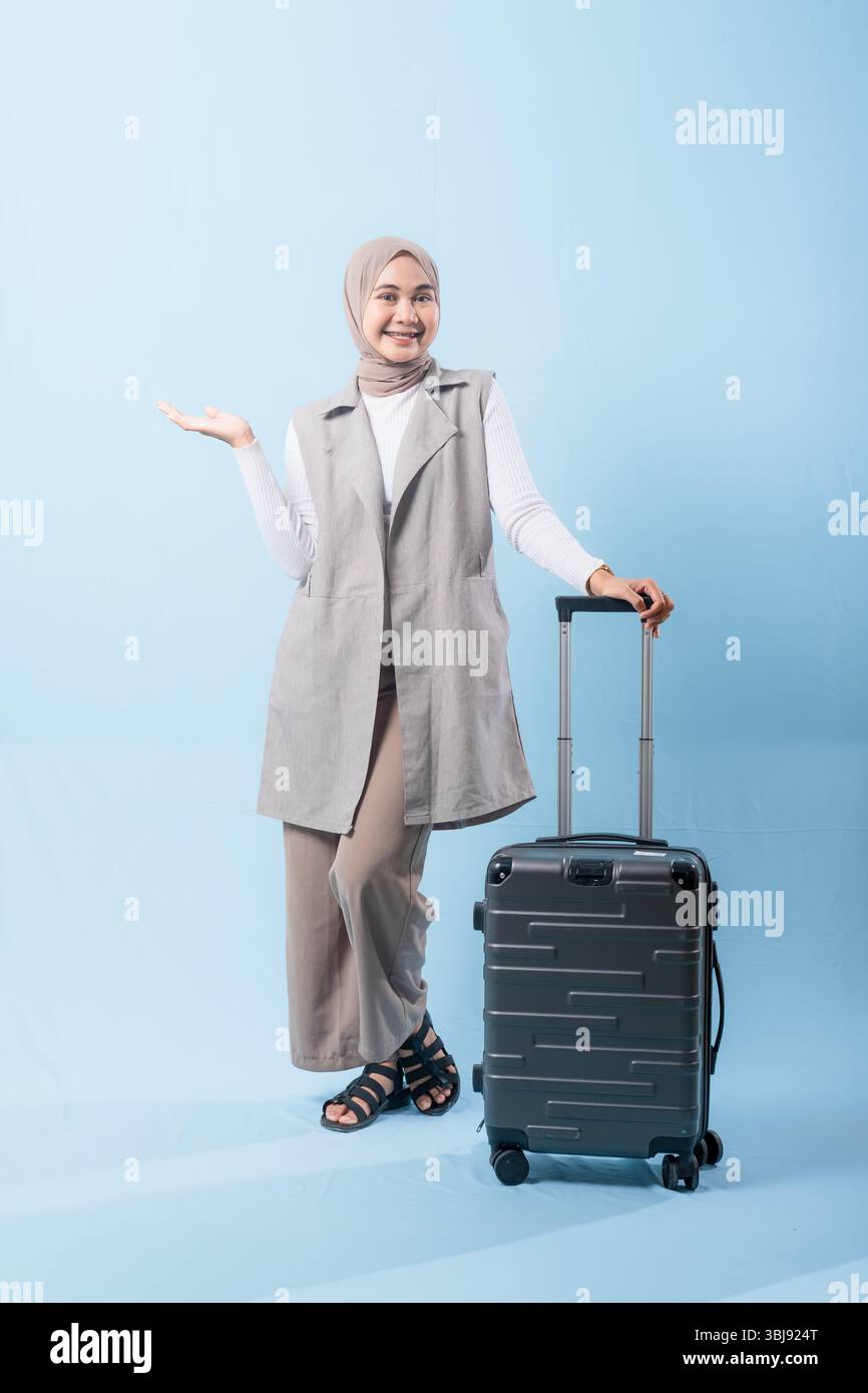 Une femme pose avec une valise, sourit et tient la main levée. Concept d'aventure et d'excitation, comme la femme est prête à se lancer dans un voyage Banque D'Images
