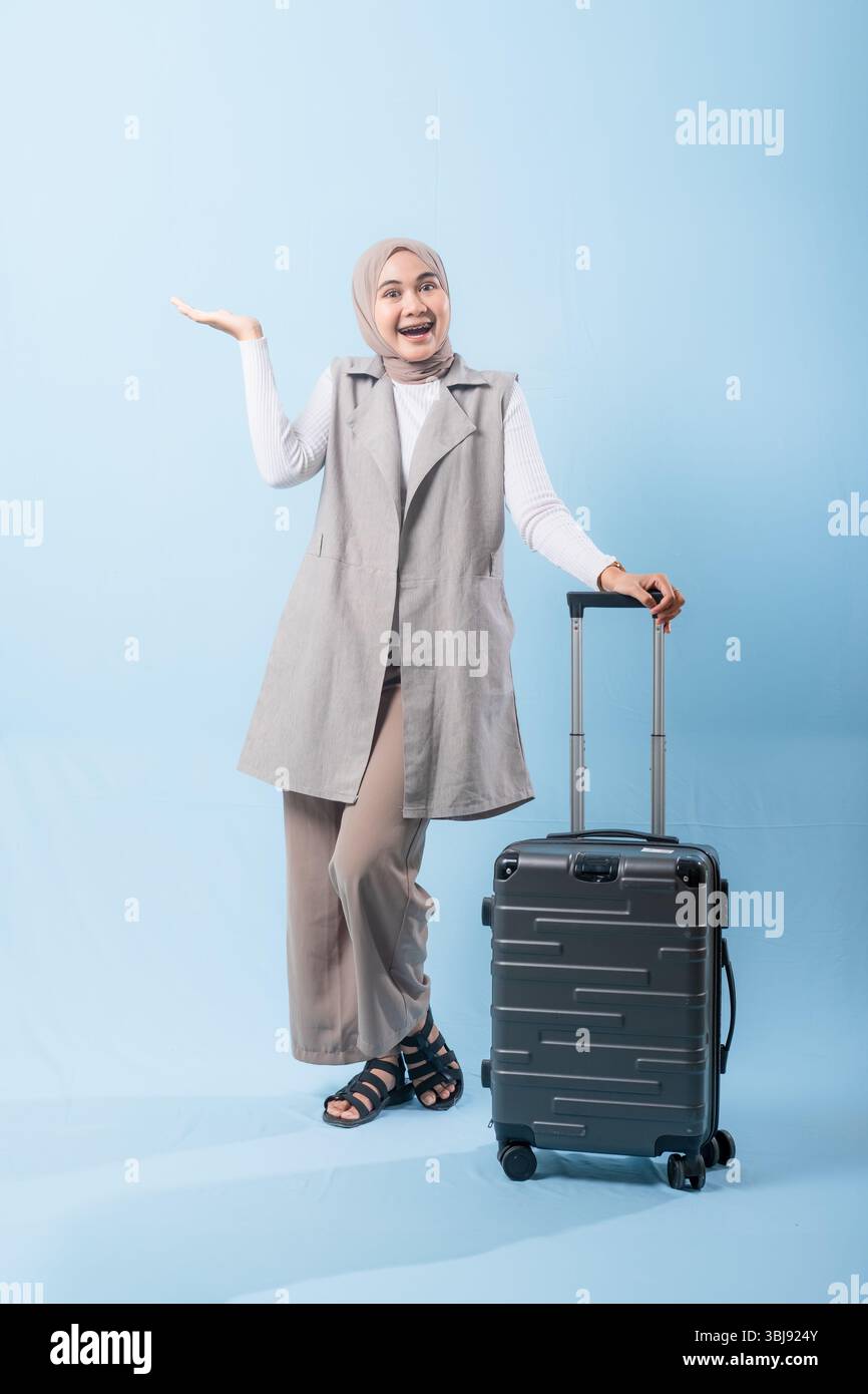 Une femme pose avec une valise, sourit et tient la main levée. Concept d'aventure et d'excitation, comme la femme est prête à se lancer dans un voyage Banque D'Images
