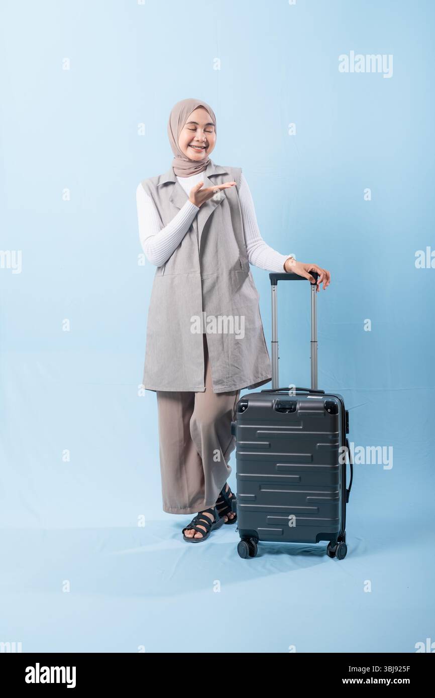 Une femme pose avec une valise, sourit et tient la main levée. Concept d'aventure et d'excitation, comme la femme est prête à se lancer dans un voyage Banque D'Images