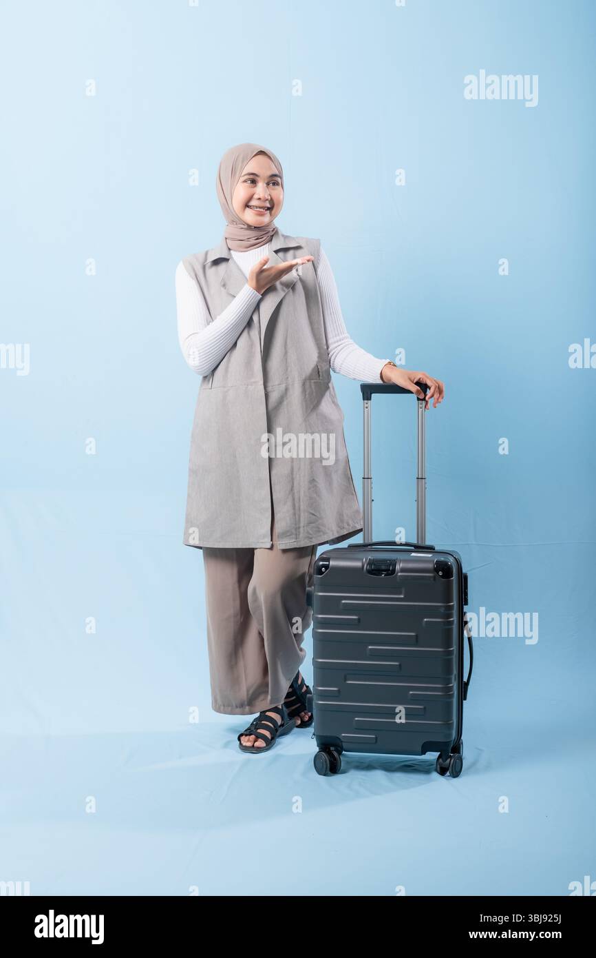 Une femme pose avec une valise, sourit et tient la main levée. Concept d'aventure et d'excitation, comme la femme est prête à se lancer dans un voyage Banque D'Images