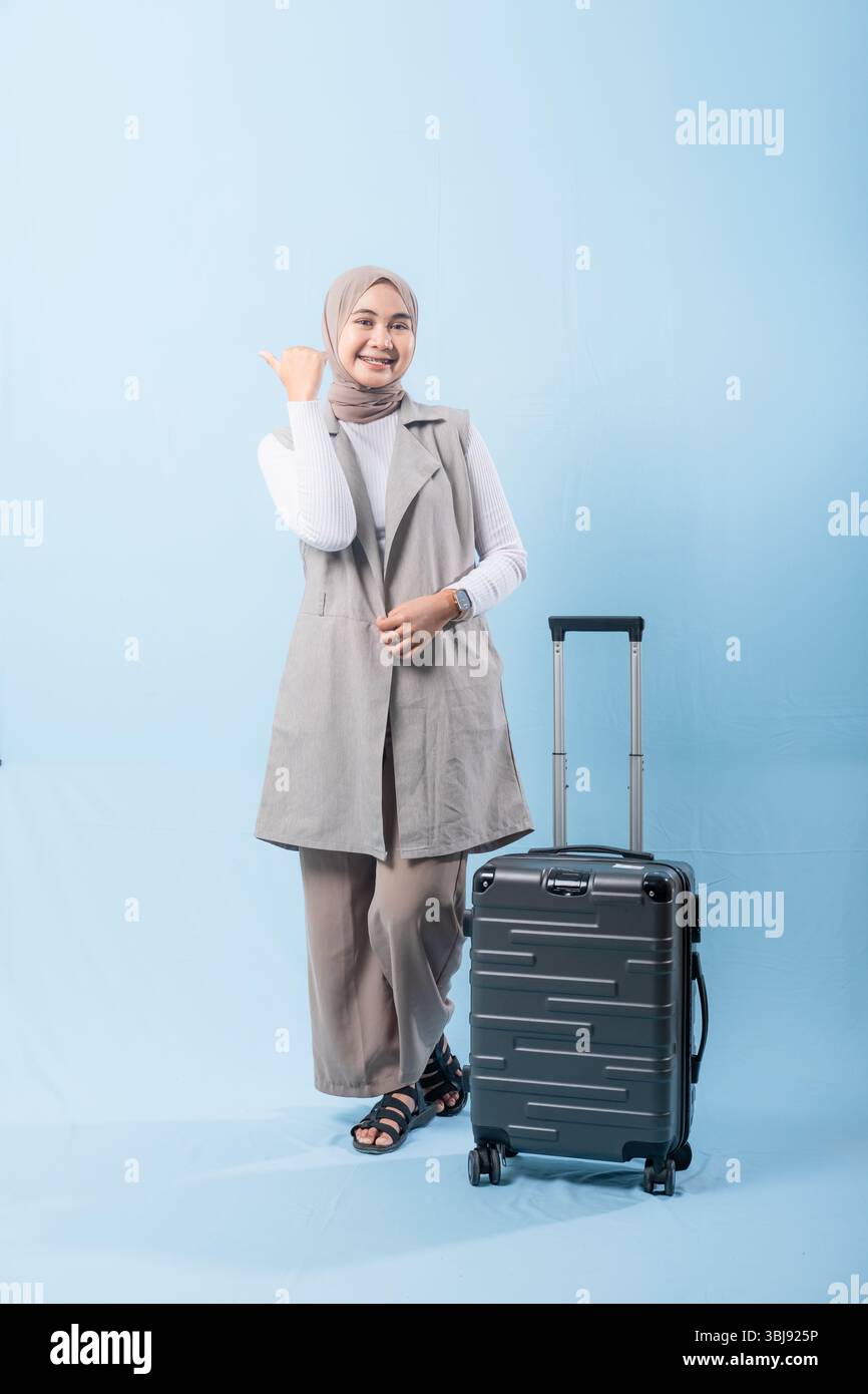 Une femme pose avec une valise, sourit et tient la main levée. Concept d'aventure et d'excitation, comme la femme est prête à se lancer dans un voyage Banque D'Images
