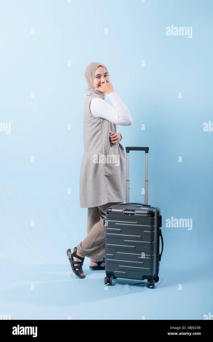 Une femme pose avec une valise, sourit et tient la main levée. Concept d'aventure et d'excitation, comme la femme est prête à se lancer dans un voyage Banque D'Images