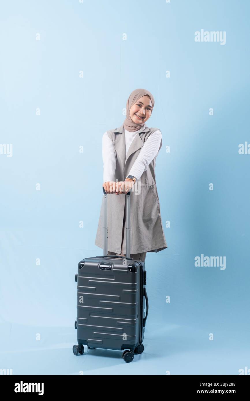 Une femme tient une valise et sourit. La valise est argentée et a des roues. La femme porte une chemise blanche et une écharpe. Concept de voyage et Banque D'Images