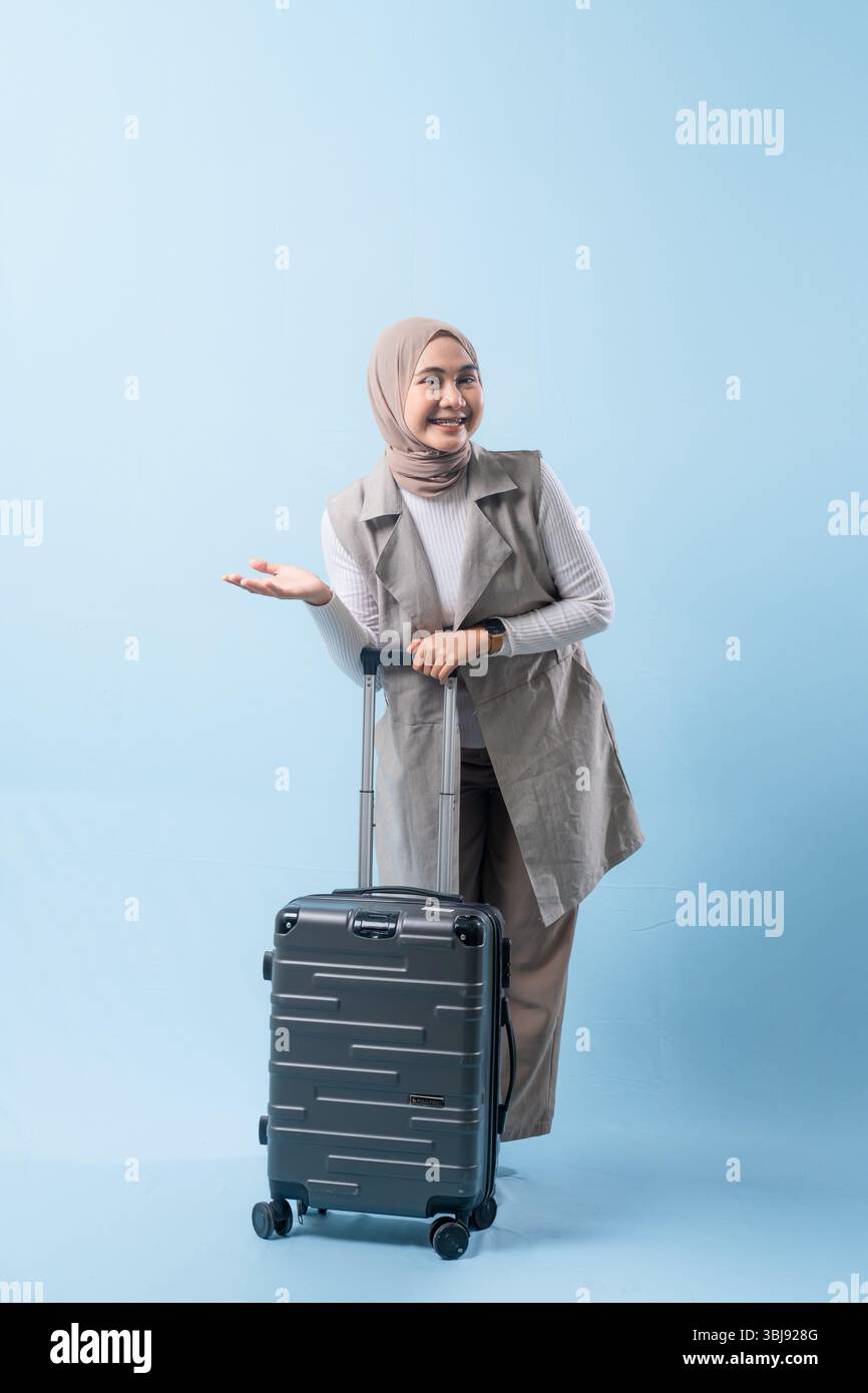 Une femme tient une valise et sourit. La valise est argentée et a des roues. La femme porte une chemise blanche et une écharpe. Concept de voyage et Banque D'Images