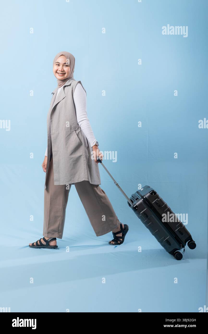 Une femme pose avec une valise, souriante et paraissant heureuse. La valise est noire et a des roues, ce qui la rend facile à transporter. Concept d'aventure Banque D'Images