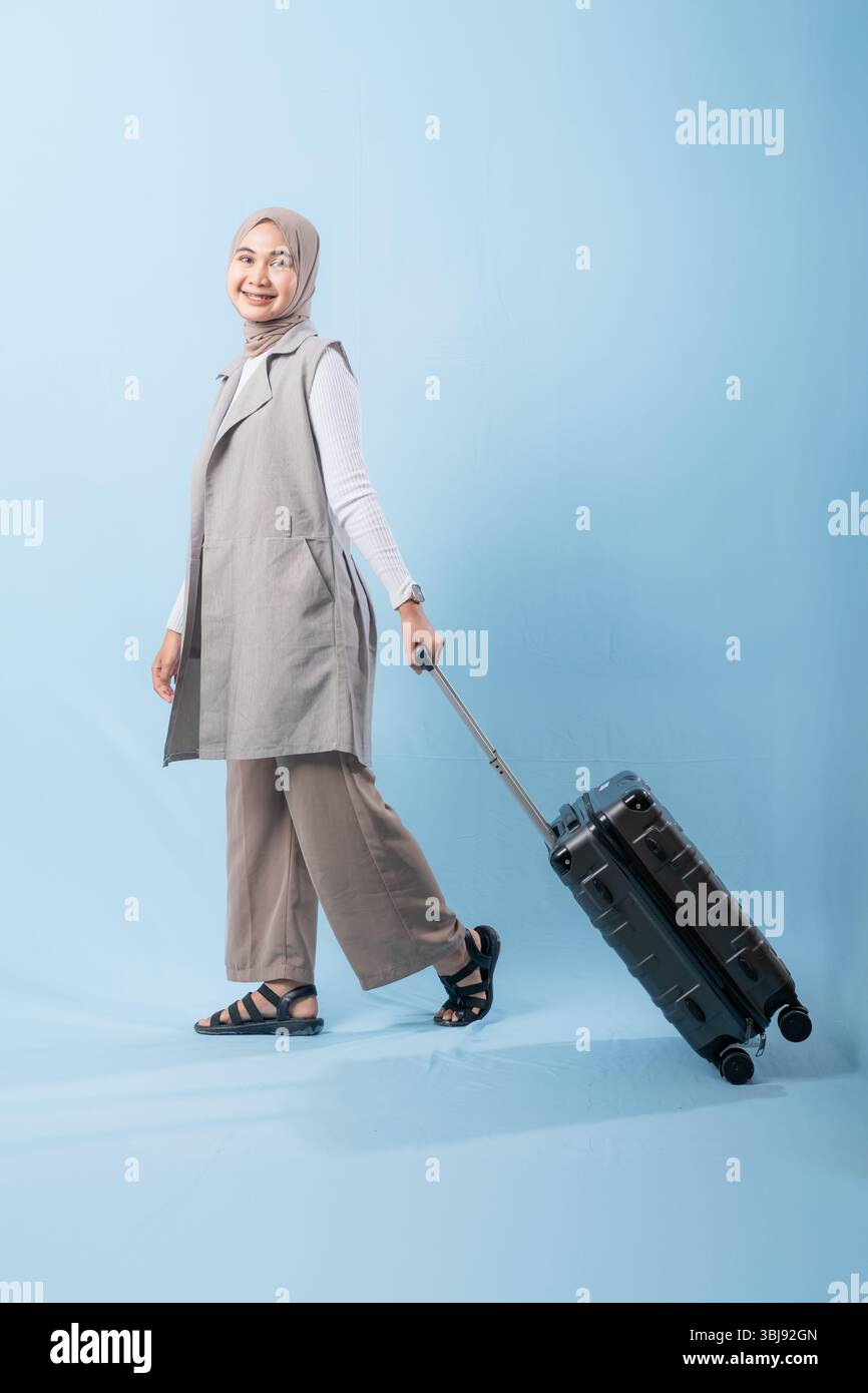 Une femme pose avec une valise, souriante et paraissant heureuse. La valise est noire et a des roues, ce qui la rend facile à transporter. Concept d'aventure Banque D'Images