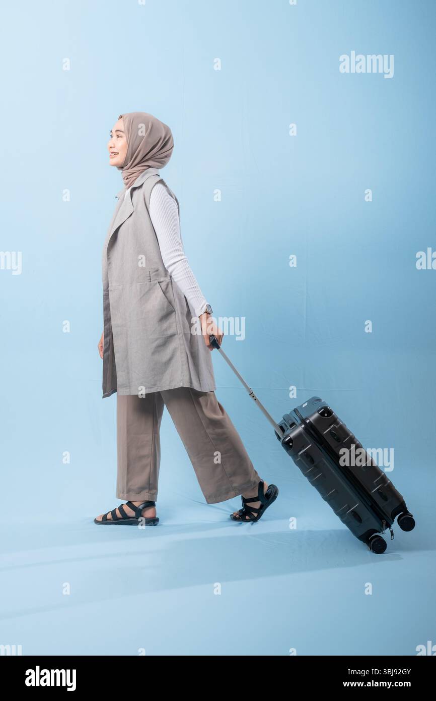Une femme pose avec une valise, souriante et paraissant heureuse. La valise est noire et a des roues, ce qui la rend facile à transporter. Concept d'aventure Banque D'Images