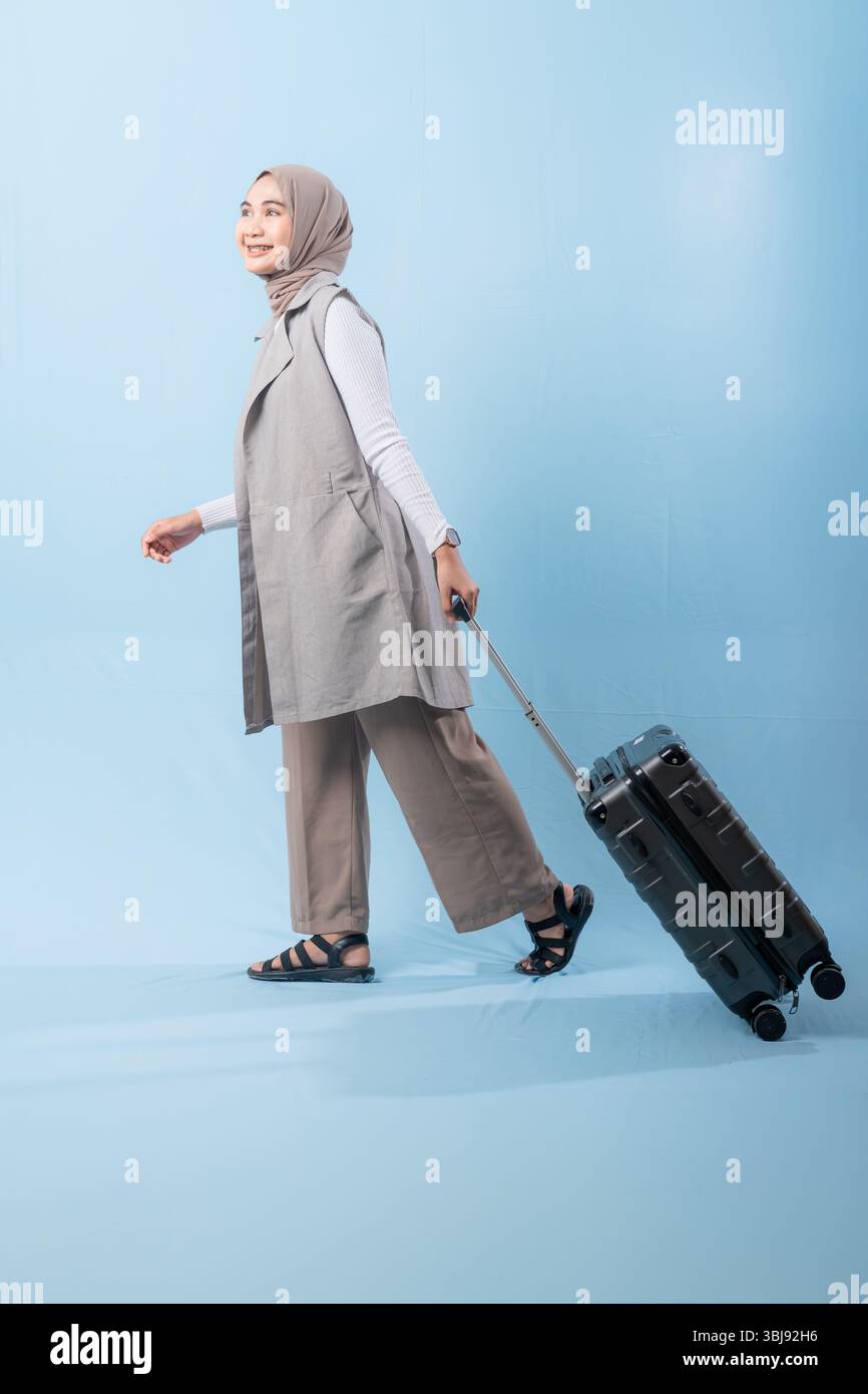 Une femme pose avec une valise, souriante et paraissant heureuse. La valise est noire et a des roues, ce qui la rend facile à transporter. Concept d'aventure Banque D'Images