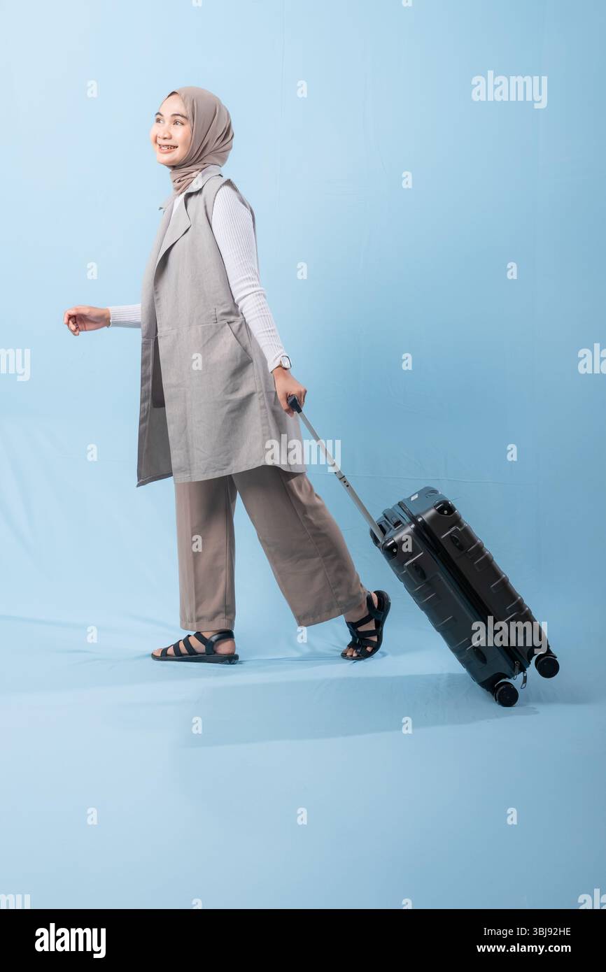 Une femme pose avec une valise, souriante et paraissant heureuse. La valise est noire et a des roues, ce qui la rend facile à transporter. Concept d'aventure Banque D'Images
