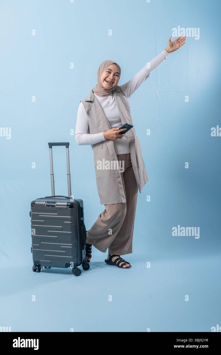 Une femme se tient debout à côté d'une valise et tient un téléphone portable. Elle sourit et elle est heureuse Banque D'Images