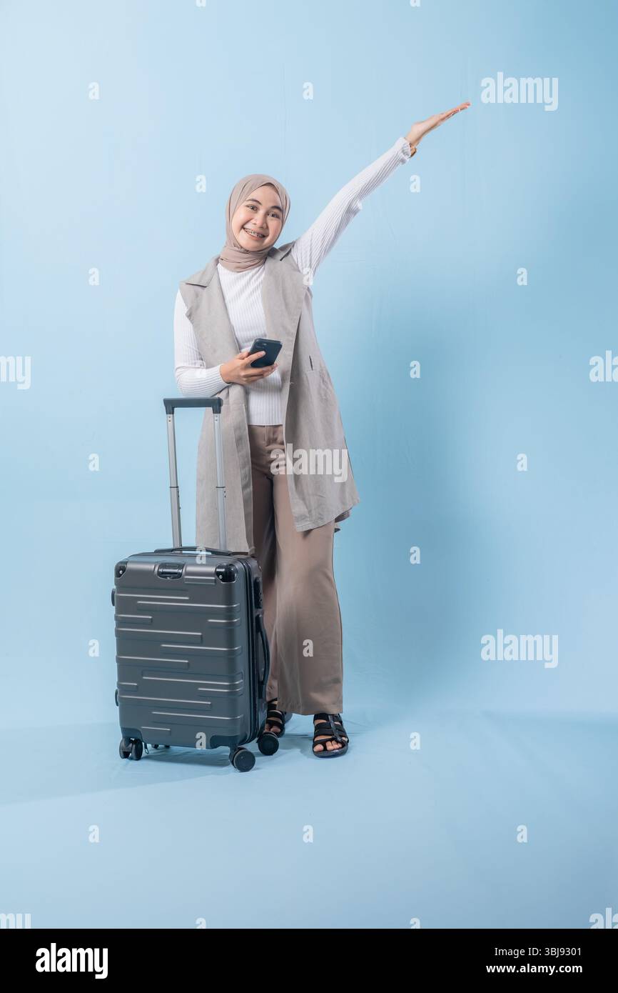 Une femme se tient debout à côté d'une valise et tient un téléphone portable. Elle sourit et elle est heureuse Banque D'Images