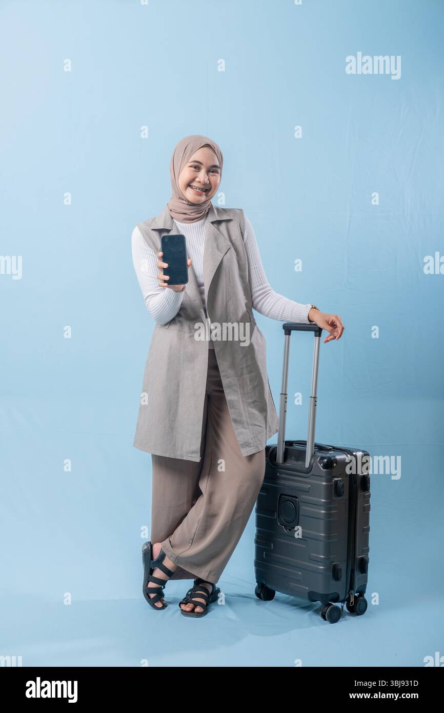 Une femme portant un foulard tient un téléphone portable et se tient debout à côté d'une valise. Concept de voyage et d'aventure, comme la femme se prépare à em Banque D'Images