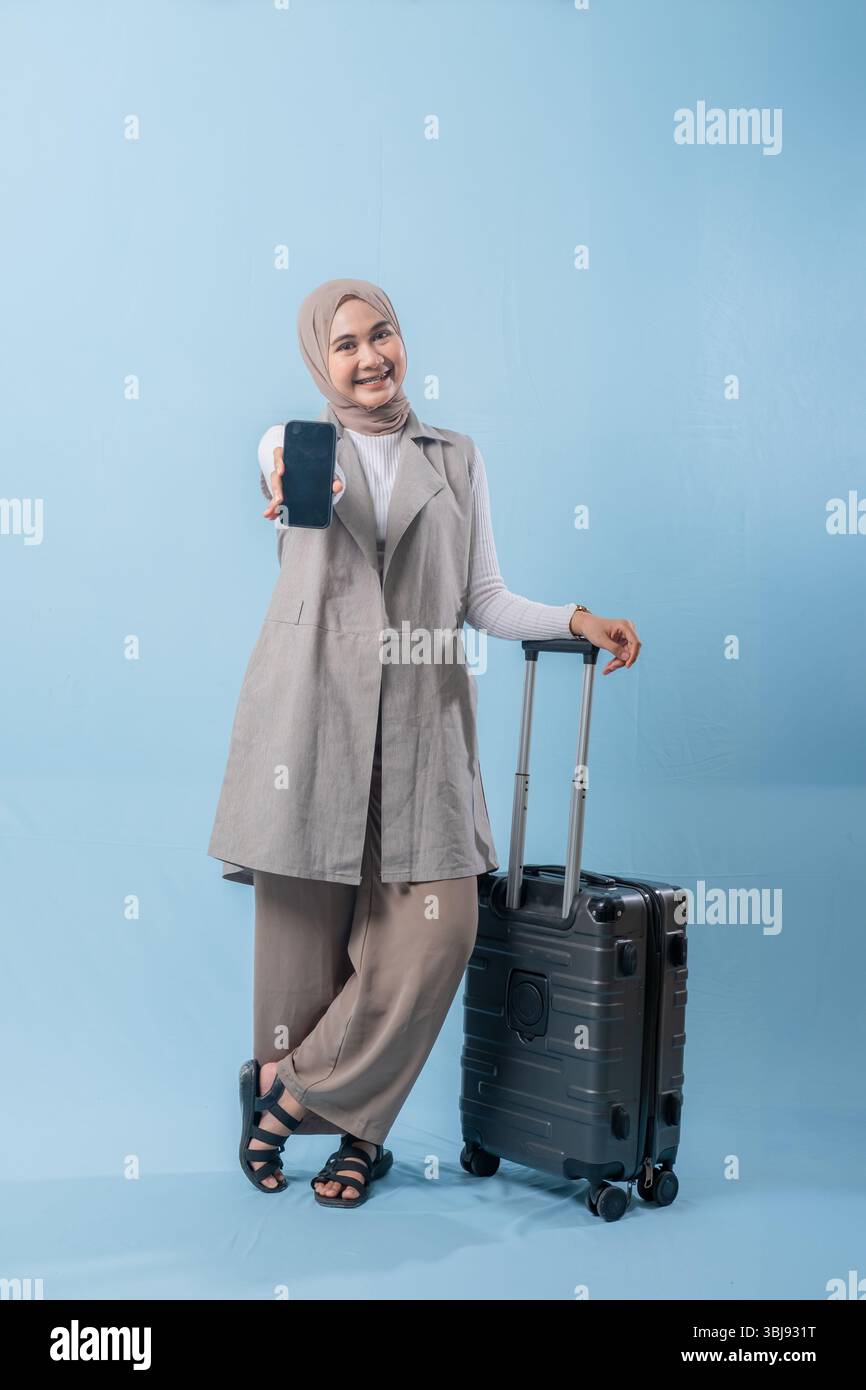 Une femme portant un foulard tient un téléphone portable et se tient debout à côté d'une valise. Concept de voyage et d'aventure, comme la femme se prépare à em Banque D'Images