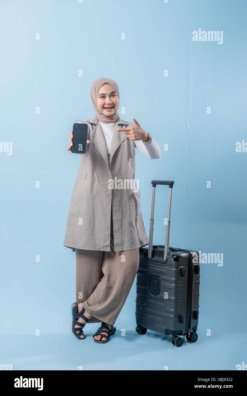 Une femme portant un foulard tient un téléphone portable et se tient debout à côté d'une valise. Concept de voyage et d'aventure, comme la femme se prépare à em Banque D'Images