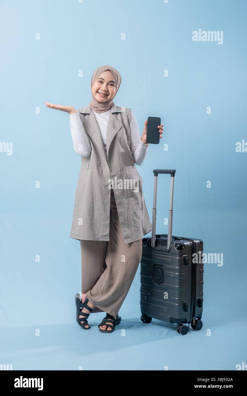 Une femme portant un foulard tient un téléphone portable et se tient debout à côté d'une valise. Concept de voyage et d'aventure, comme la femme se prépare à em Banque D'Images