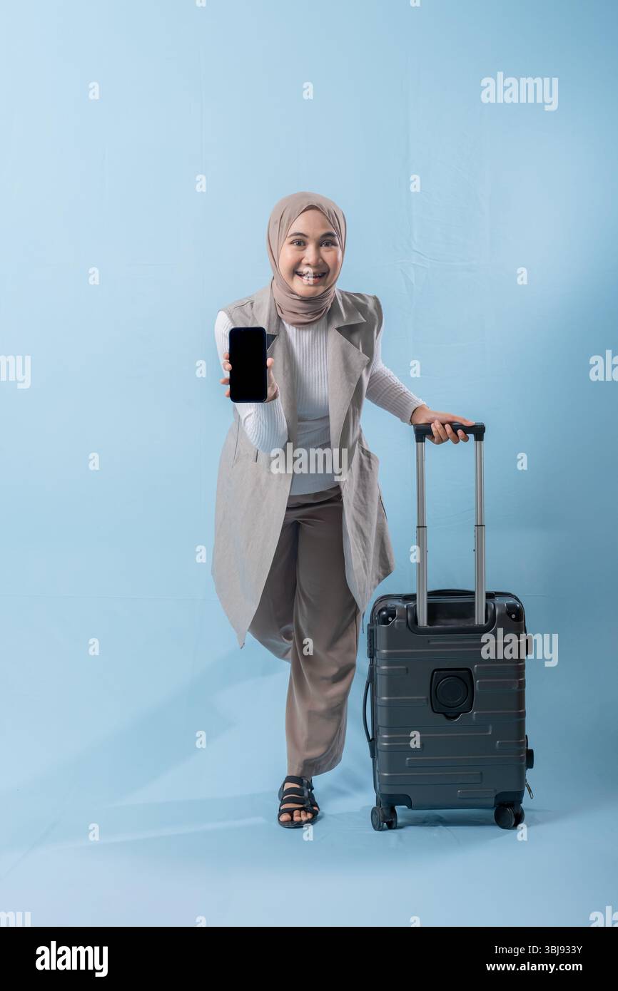 Une femme portant un foulard tient un téléphone portable et se tient debout à côté d'une valise. Concept de voyage et d'aventure, comme la femme se prépare à em Banque D'Images