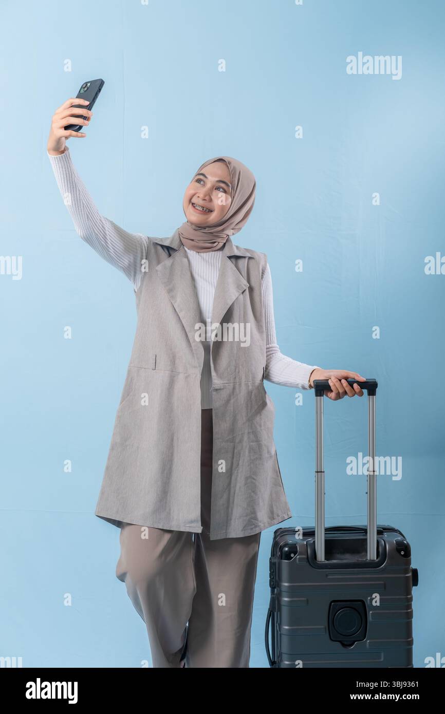 Une femme prend un selfie avec son téléphone tout en tenant une valise. Concept de voyage et d'aventure, alors que la femme se prépare à se lancer dans un voyage. Banque D'Images