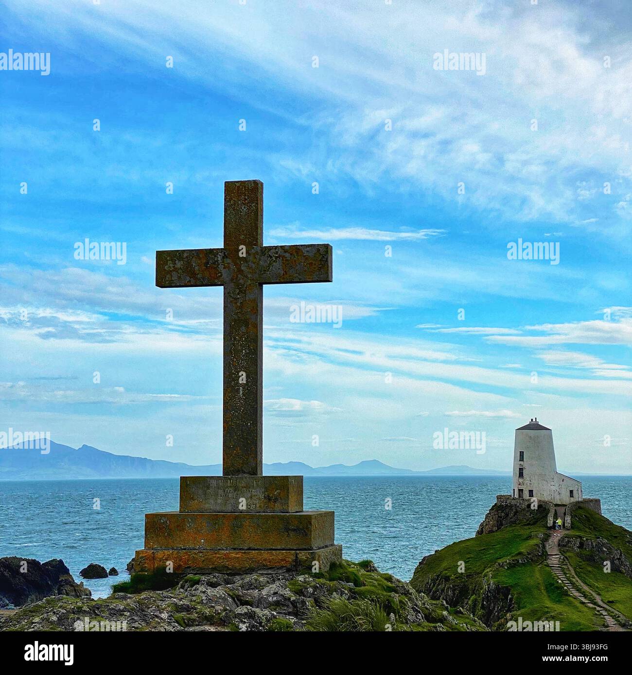 Croix de pierre sur Ynys Llandwyn avec phare et montagnes de Snowdonia à distance sous ciel bleu vif et nuages blancs tortueux - Image de stock capturée avec un smartphone