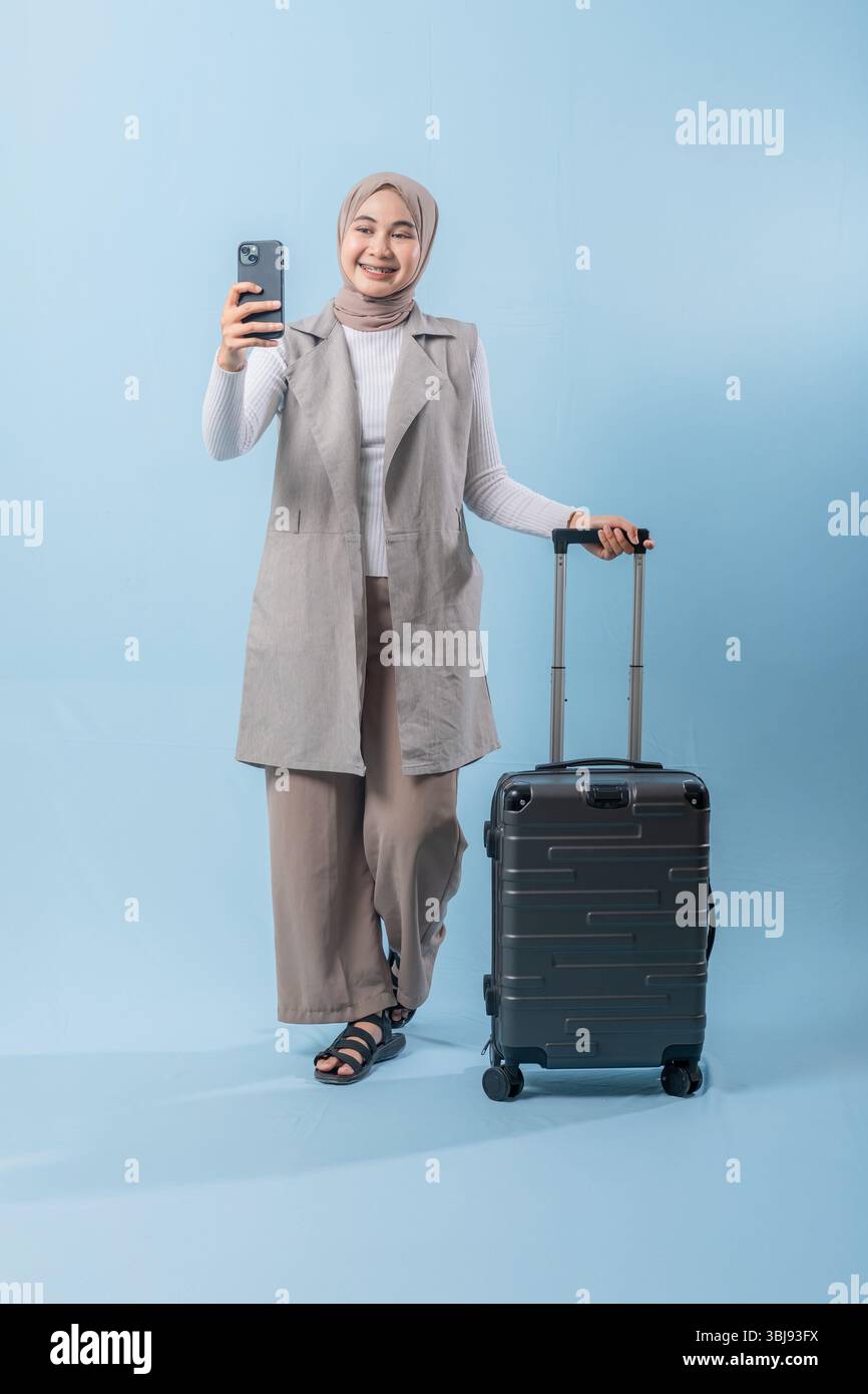 Une femme prend un selfie avec son téléphone tout en tenant une valise. Concept de voyage et d'aventure, alors que la femme se prépare à se lancer dans un voyage. Banque D'Images
