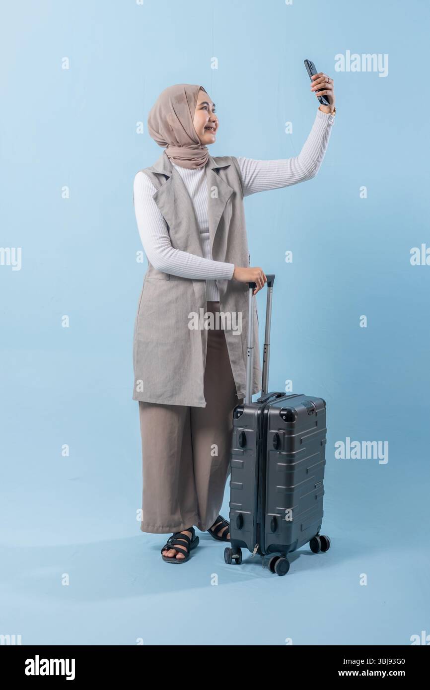 Une femme prend un selfie avec son téléphone tout en tenant une valise. Concept de voyage et d'aventure, alors que la femme se prépare à se lancer dans un voyage. Banque D'Images