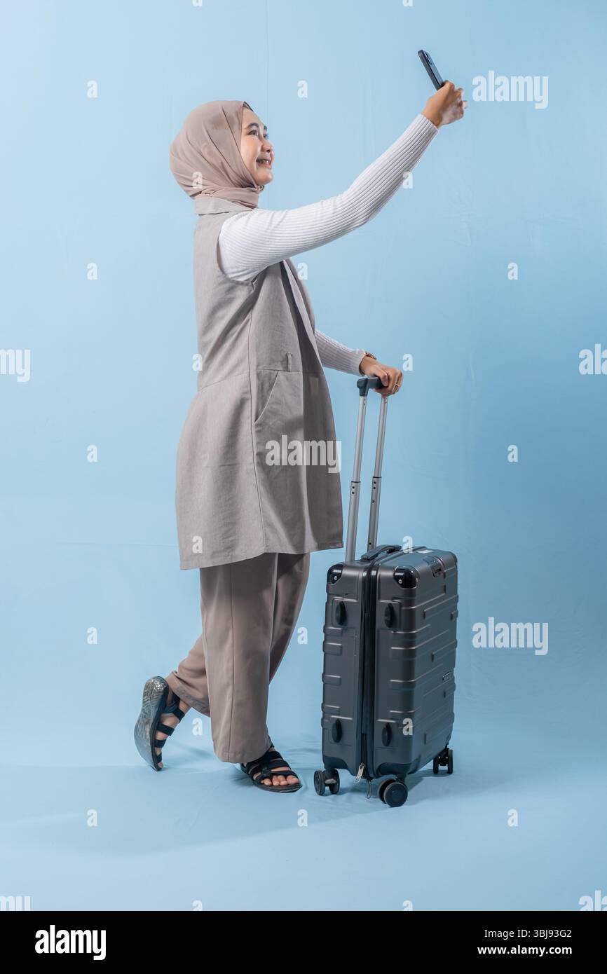 Une femme prend un selfie avec son téléphone tout en tenant une valise. Concept de voyage et d'aventure, alors que la femme se prépare à se lancer dans un voyage. Banque D'Images
