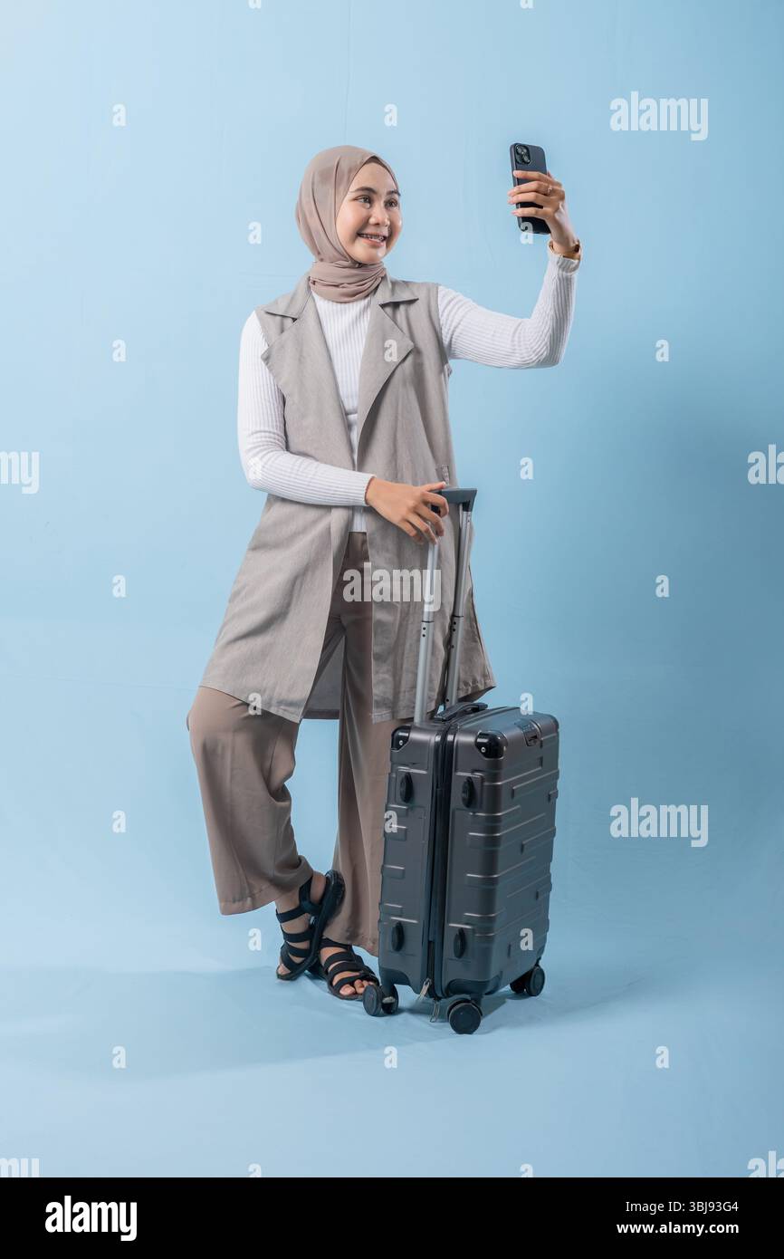 Une femme prend un selfie avec son téléphone tout en tenant une valise. Concept de voyage et d'aventure, alors que la femme se prépare à se lancer dans un voyage. Banque D'Images