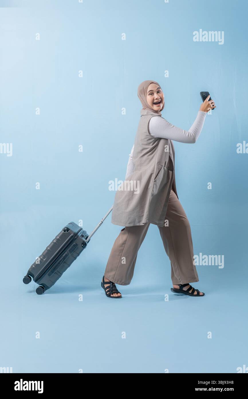 Une femme marche avec une valise et sourit. Elle tient un téléphone portable, et elle prend un selfie. Concept de voyage et d'aventure, ainsi que Banque D'Images