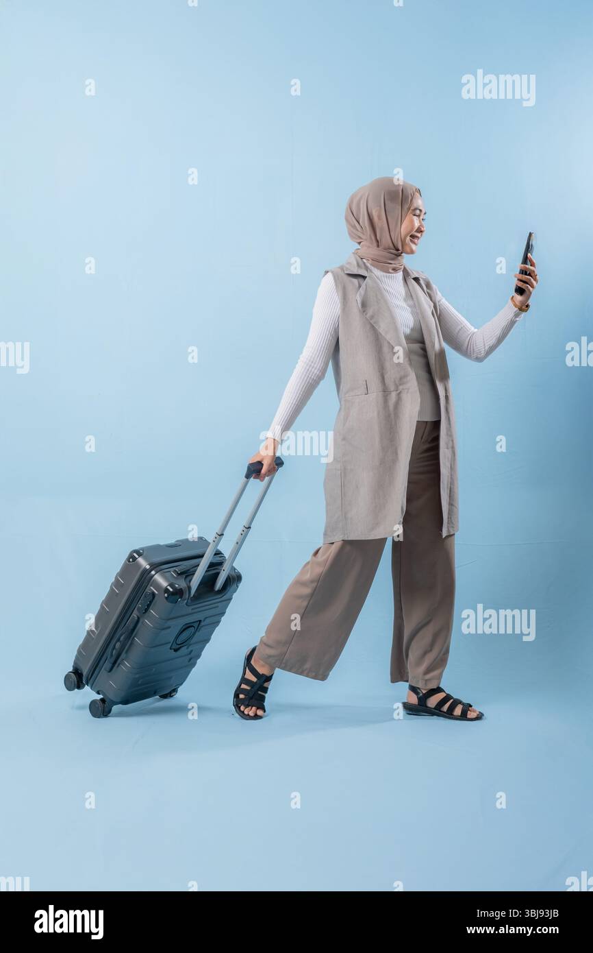Une femme marche avec une valise et sourit. Elle tient un téléphone portable, et elle prend un selfie. Concept de voyage et d'aventure Banque D'Images