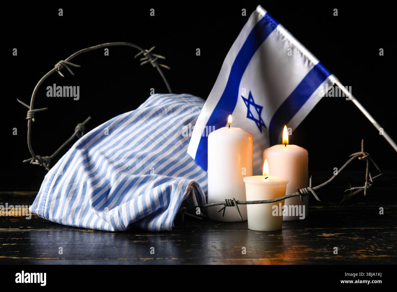 Uniforme de prisonnier, bougies allumées, fil de fer barbelé et drapeau d'Israël sur fond sombre. Jour du souvenir de l'Holocauste Banque D'Images