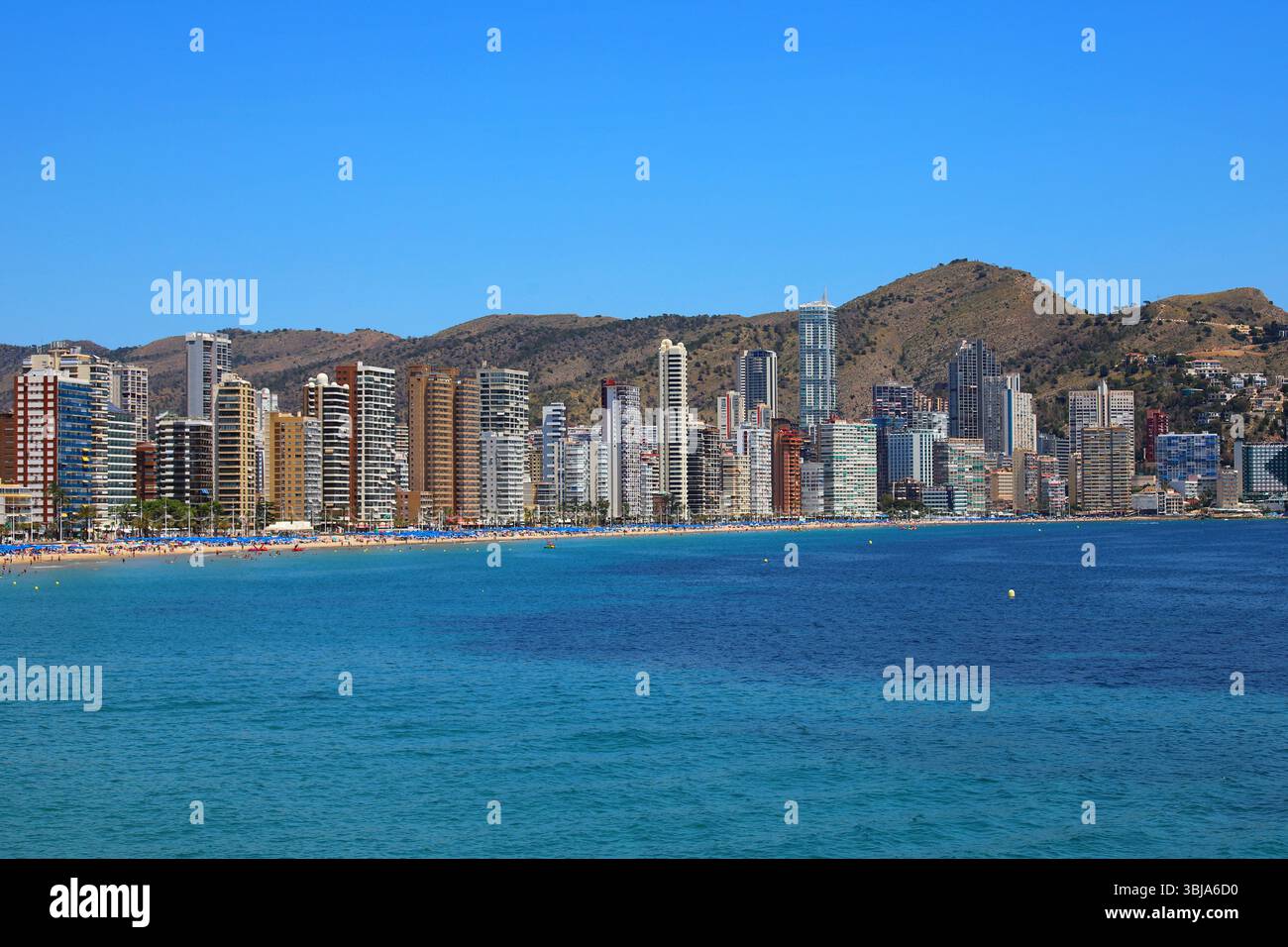 Levante Beach de Benidorm, Espagne, avec une mer turquoise, des bains de soleil et une ligne d'horizon dense de gratte-ciel modernes dans un fond montagneux. Banque D'Images