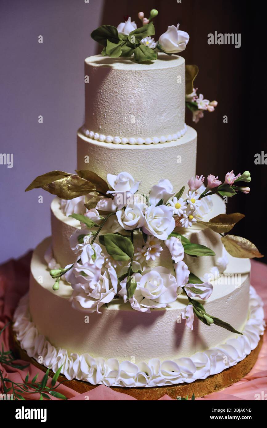 Élégant gâteau de mariage blanc à quatre niveaux décoré de belles fleurs blanches et de feuilles vertes. Dessert de luxe pour une célébration ou un mariage Banque D'Images
