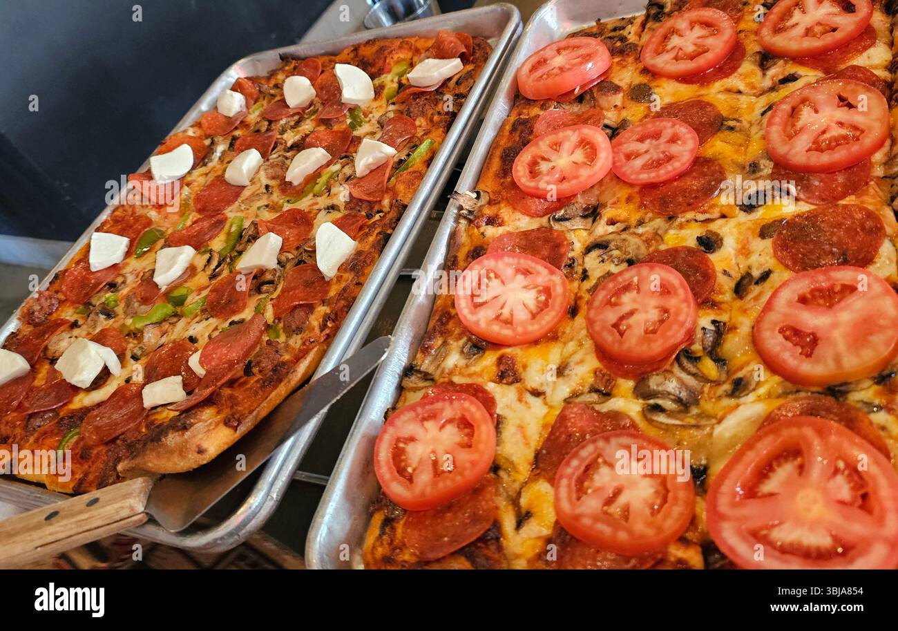 Deux pizzas poêlées, saucisse pepperoni, champignons et tranches de tomates fraîches, poivrons verts et saucisse avec garniture de mozarella fraîche. Banque D'Images
