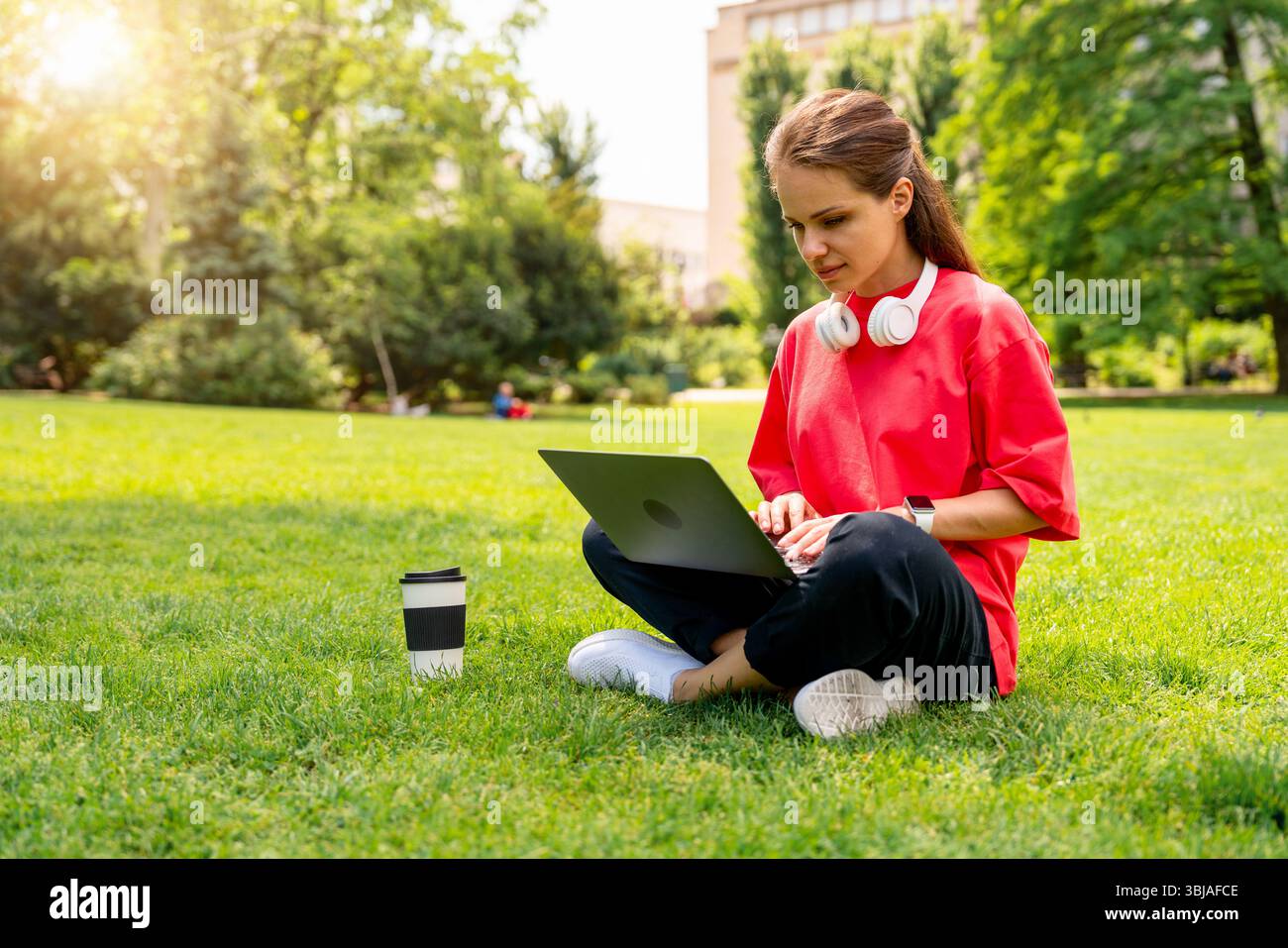 Jeune femme travaillant à distance avec un ordinateur portable dans un parc urbain Banque D'Images