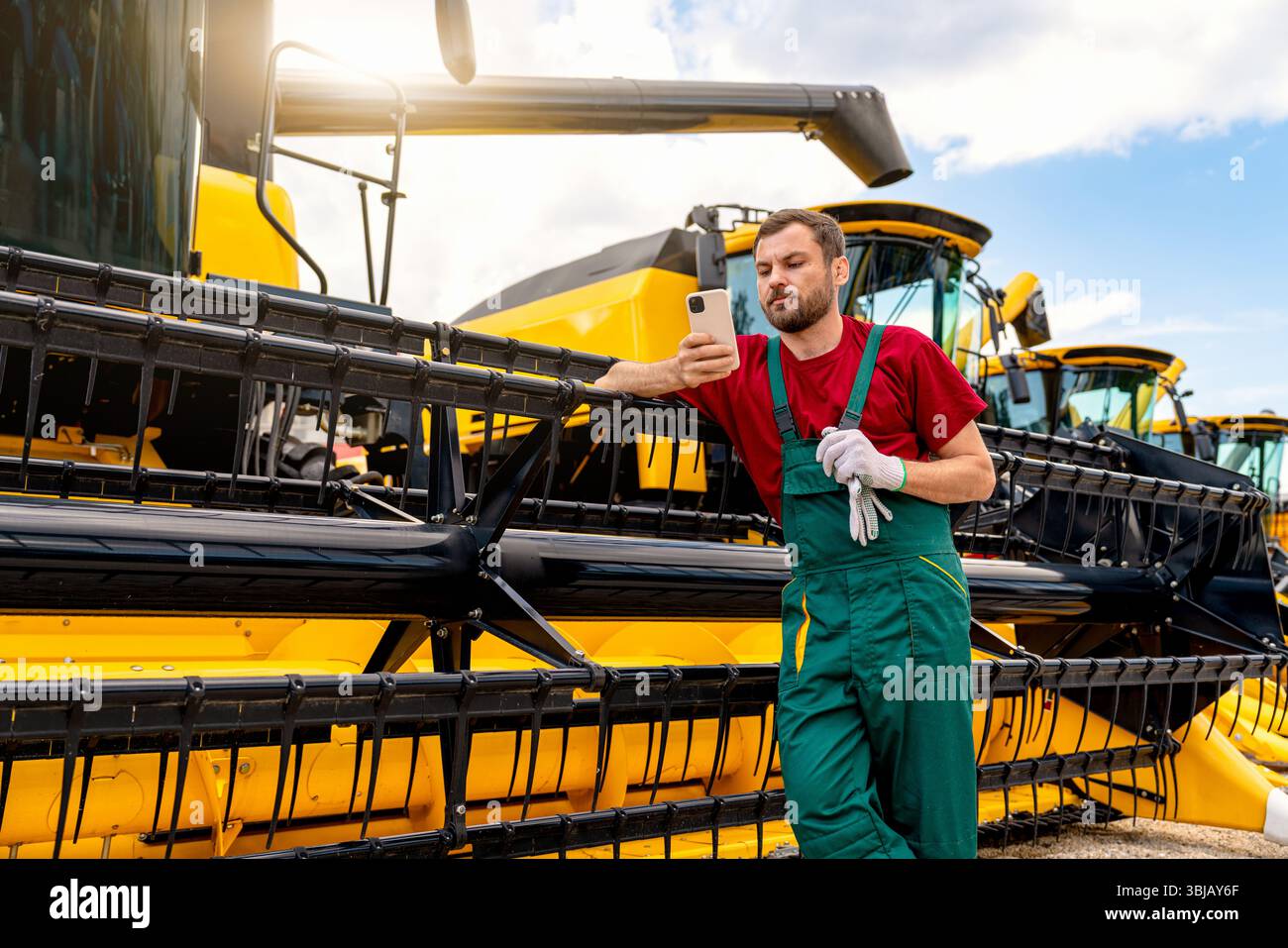 Opérateur de moissonneuse-batteuse utilisant un smartphone près de la récolteuse dans la cour d'équipement Banque D'Images