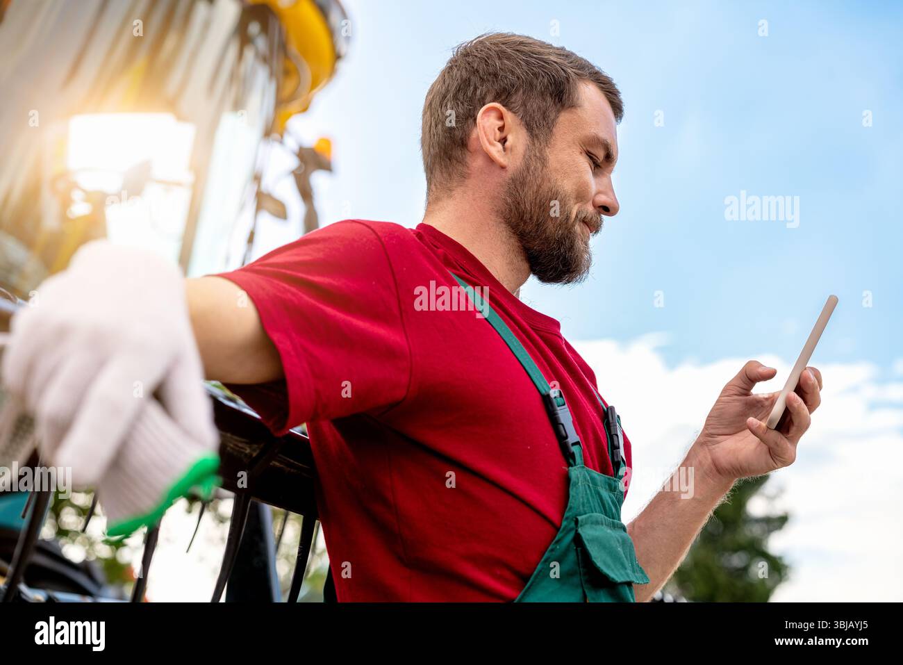 Ouvrier agricole souriant à l'aide d'un smartphone près de la moissonneuse-batteuse Banque D'Images