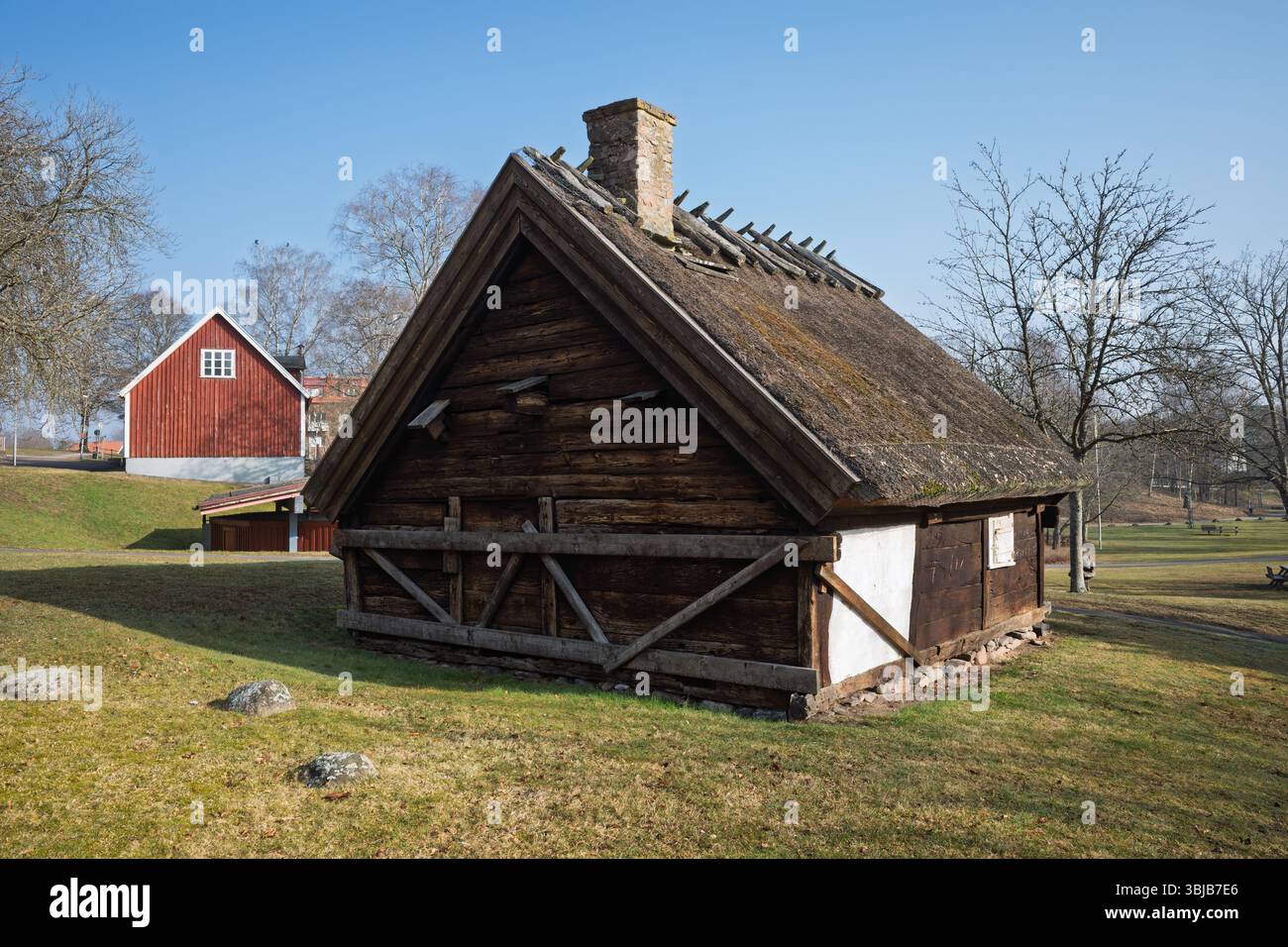 Un chalet traditionnel en bois avec un toit de chaume distinctif et une cheminée en briques se dresse sur une colline herbeuse à Hässleholm, en Suède. Banque D'Images