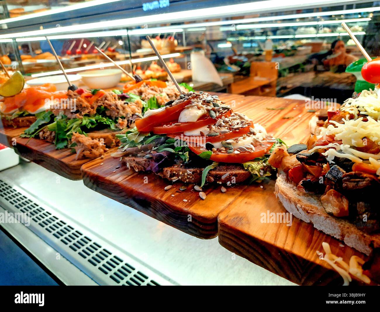Assortiment de sandwichs ouverts recouverts d'ingrédients comme le thon, la tomate, le saumon, le fromage et les graines sur du pain rustique, présentés sur des planches de bois à l'intérieur d'un puits Banque D'Images