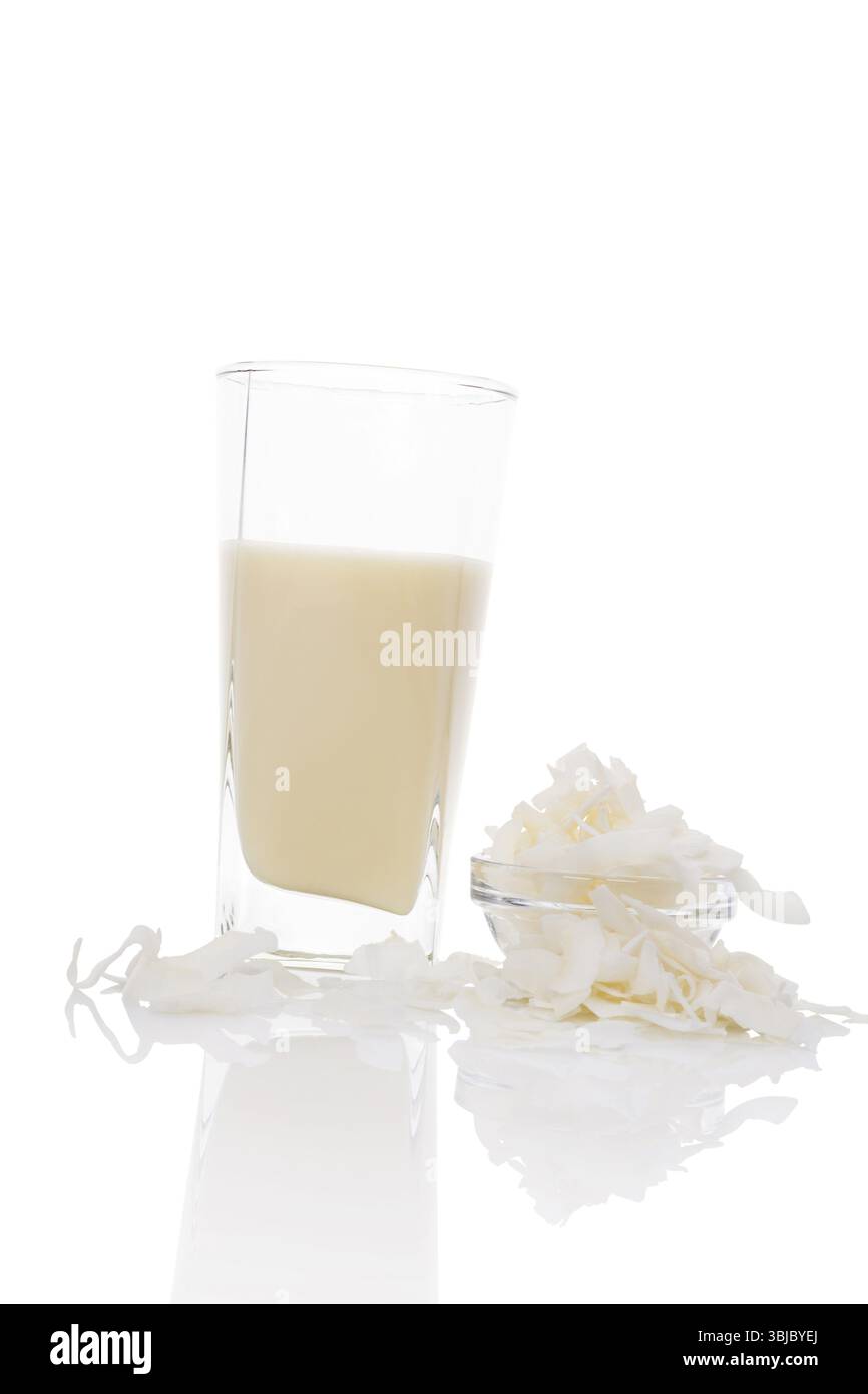 Lait de coco en verre avec des flocons de noix de coco dans un bol en verre isolé sur fond blanc. Concept de lait végétalien et végétarien Banque D'Images