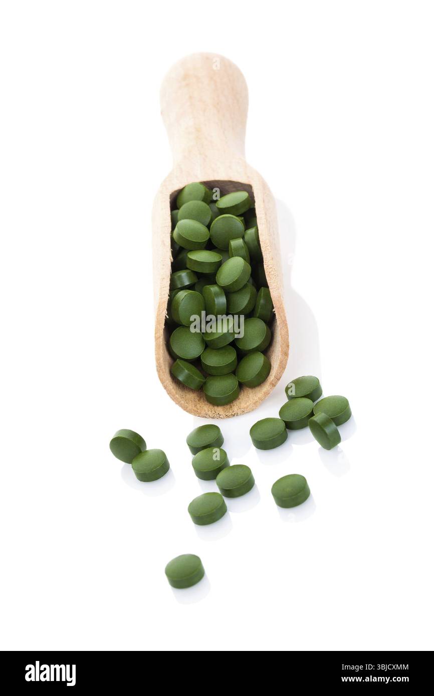 Pilules vertes sur cuillère en bois isolé sur fond blanc avec réflexion. Spiruline, chlorella et wheatgrass. Concept de vie saine Banque D'Images